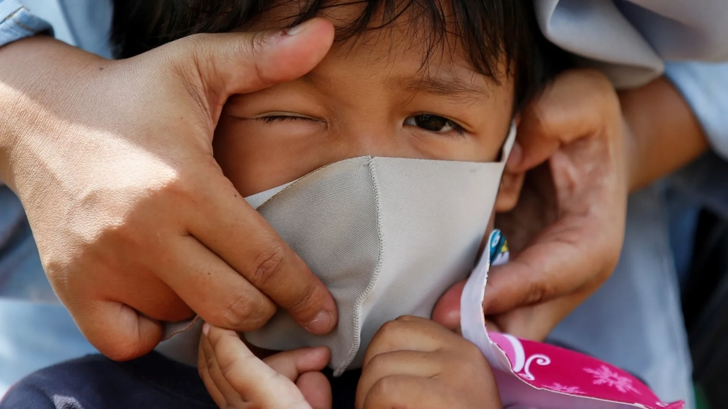 A family member puts a face mask on a child in Jakarta during the coronavirus outbreak [Willy Kurniawan/Reuters]
