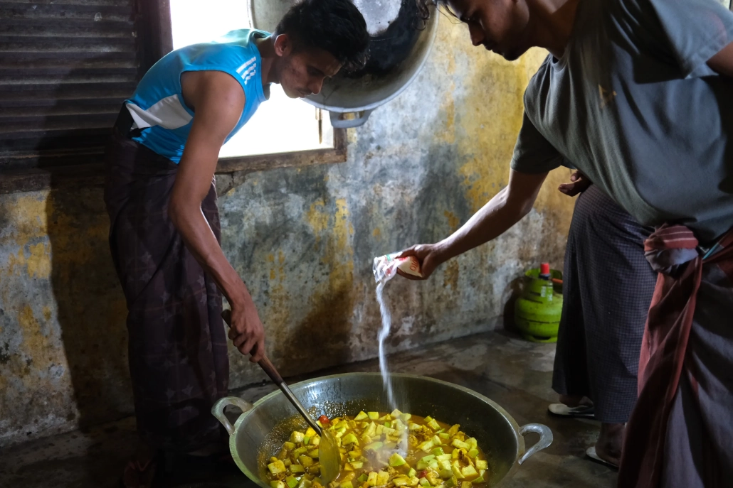 Preparing lunch is a communal activity, with several people working together even on just one dish. These men are cooking a dish called salong, a traditional curry. [Jessica Washington/Al Jazeera]