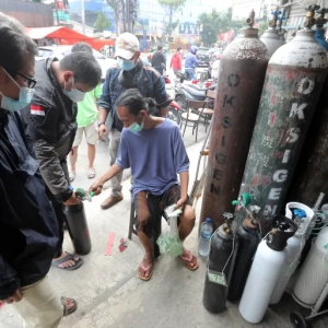 A worker checks the queue number at an oxygen refill shop in Jakarta. The surge in COVID-19 cases has led to soaring demand for oxygen [Bagus Indahono/EPA]