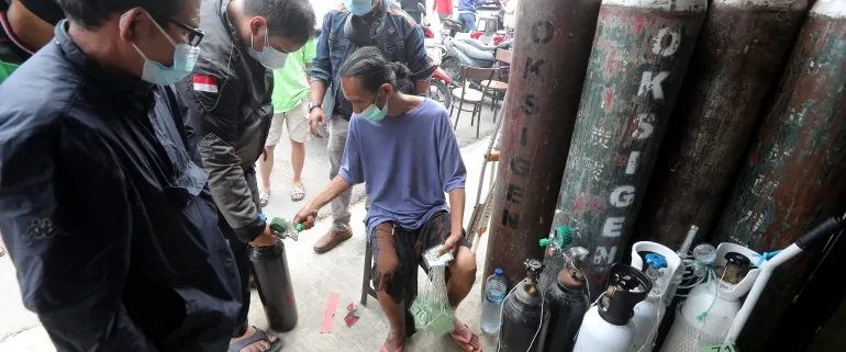 A worker checks the queue number at an oxygen refill shop in Jakarta. The surge in COVID-19 cases has led to soaring demand for oxygen [Bagus Indahono/EPA]