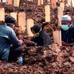 Families mourn at the graveside of a loved one lost to COVID-19 [Fakhrur Rozi/Al Jazeera]